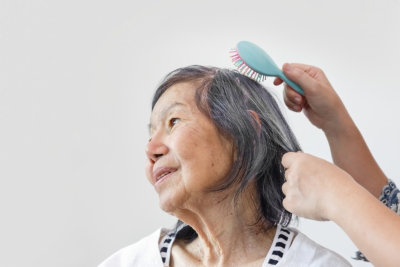 a person combing the hair of senior woman 